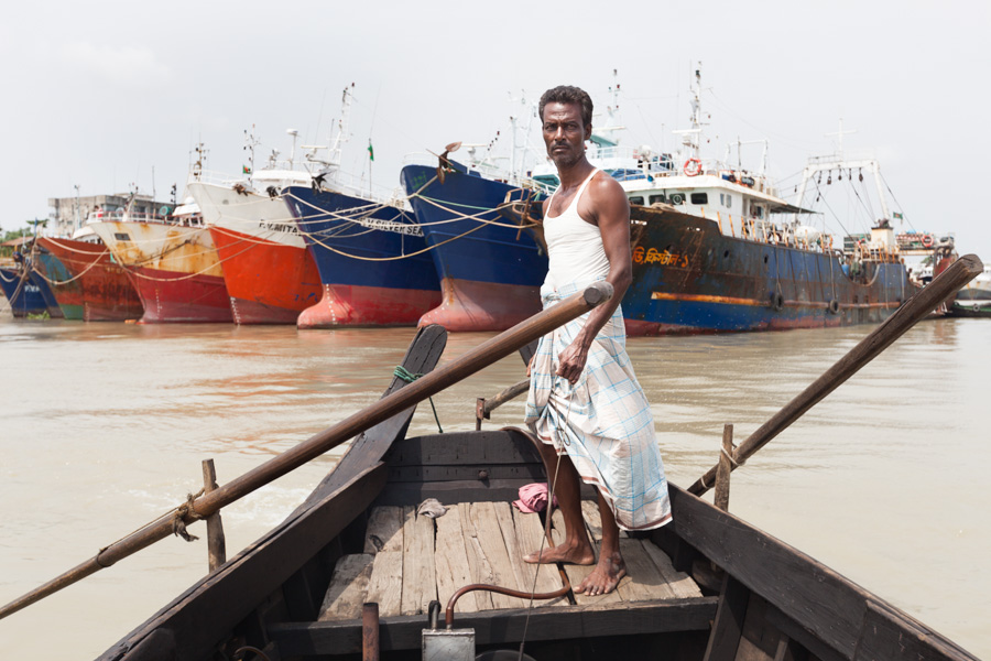 Bangladeshi boatman rowing his boat in front of old big ships near Sadarghat (River port) at Karnaphuli (Karnafuli) River, Chittagong, Bangladesh, Indian Sub-Continent, Asia