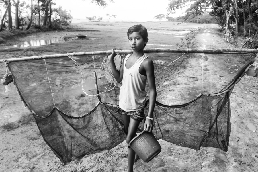 Boy with a fishing net and a bucket in his hands going to the river, Fishermen settlement near Chamdomban village, East Side of Kirtonkhola River, Barisal, Barisal District, Bangladesh, Indian Sub-Continent, Asia.