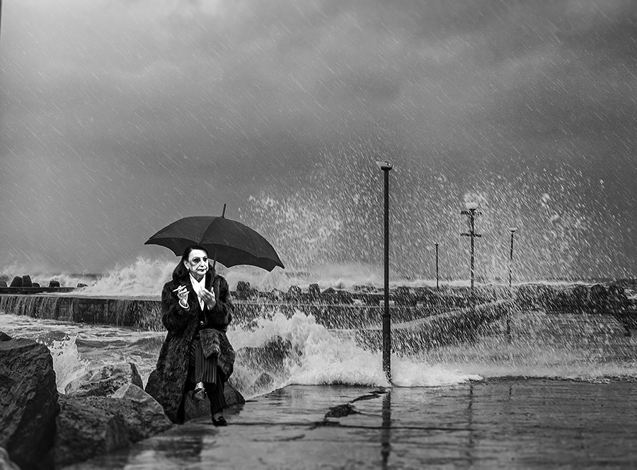 A sophisticated lady sitting on a stone and smoking cigarette during a severe sea storm.