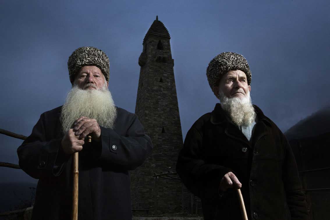 Two elders of Vedeno highland region in Chechnya pose by the ancestry tower, ruined by the Soviets and rebuilt anew upon their return from exile.