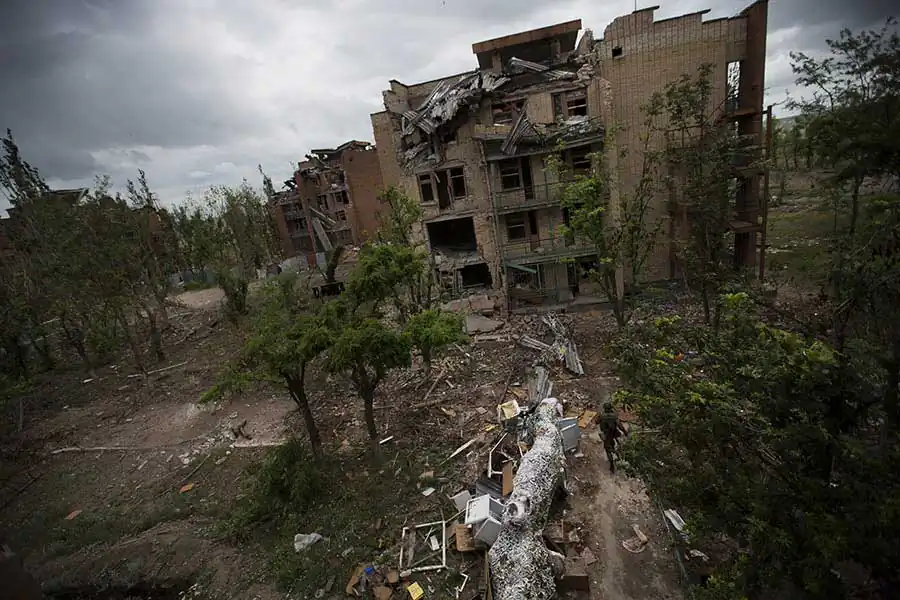 A fighter of "Donbas" battalion dodging sniper' bullets beside a ruin of ex-sanatorium, destroyed by the Russian artillery, June 26 2015, Shirokino, East of Ukraine