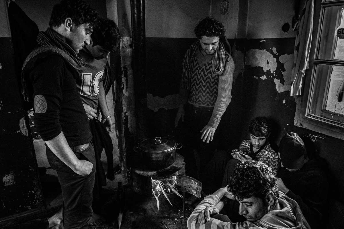Inside abandoned building, migrants prepare meal together.